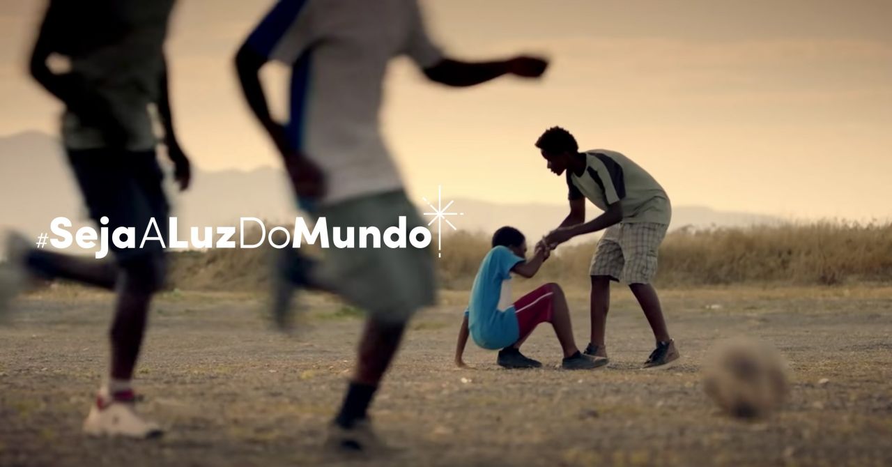 Um menino ajuda outro menino a se levantar após ter caído jogando futebol no vídeo Seja a Luz do Mundo