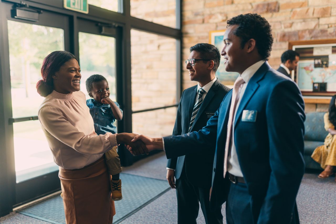 Dois missionários cumprimentam uma mulher segurando uma criança na Igreja